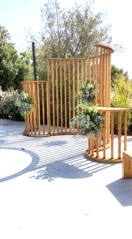 Estructura de madera con plantas, situada en un espacio al aire libre iluminado.