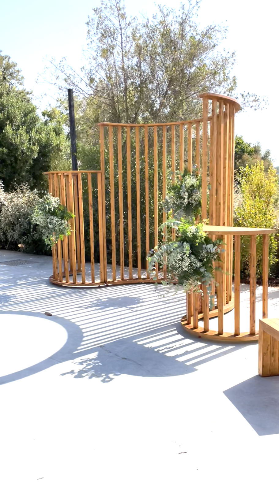 Waves Estructura de madera con plantas, situada en un espacio al aire libre iluminado.